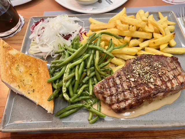 rechteckiger Teller mit Salat, Bohnen, Pommes, Knoblauchbrit und einem Steak auf hellbrauner Sauce