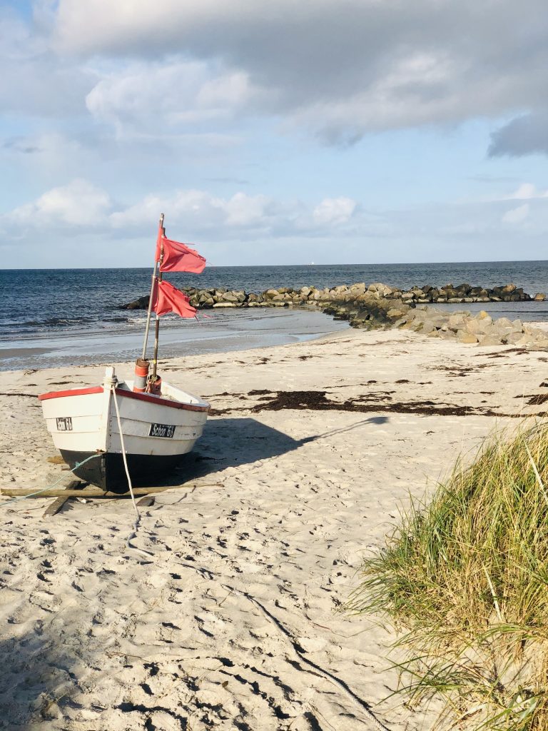 Strand mit einem Ruderboot auf dem Sand, im Hintergrund eine Buhne, die Ostsee und bewölkter Himmel
